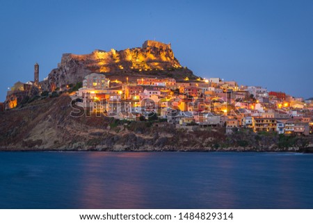 Colorful houses on the hillside with a fortress on the top. Night panorama of medieval town Castelsardo, Sardinia, Italy. Beautiful, calm evening. Popular touristic destination. 
