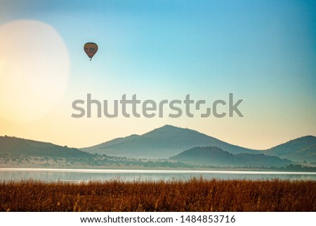 A hot air balloon hovering high in the sky, above Mankwe Dam, in Pilanesberg Nature Reserve, South Africa. Photo taken at sunrise with lens flare.