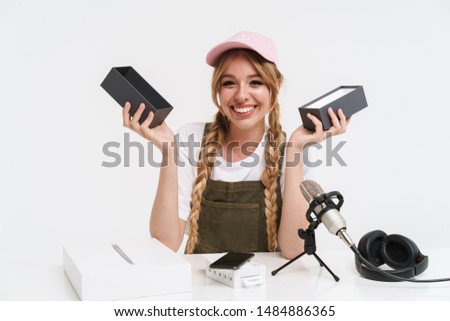 Image of positive girl recording blog broadcast with microphone about new smartphone isolated over white wall in studio