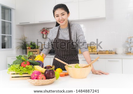 Portrait of beautiful asian woman is standing in the bright white kitchen. wife or housewife is preparing to cook healthy food which consists of a variety of fruits and vegetables for the family. Royalty-Free Stock Photo #1484887241