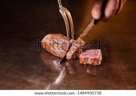 Japanese chef is cooking by hand a sliced delicious Kobe Beef or Wagyu steak in Teppanyaki style. Hot and delicious roast-beef, fesa, ranichi Royalty-Free Stock Photo #1484900738