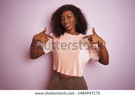 Young african american woman wearing t-shirt standing over isolated pink background looking confident with smile on face, pointing oneself with fingers proud and happy.