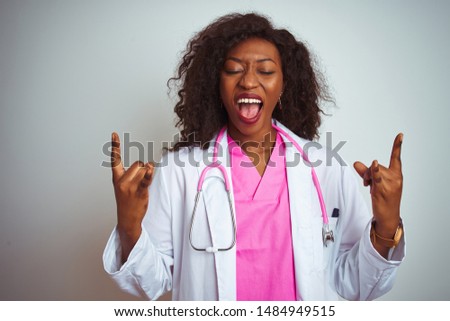 African american doctor woman wearing  pink stethoscope over isolated white background shouting with crazy expression doing rock symbol with hands up. Music star. Heavy concept.