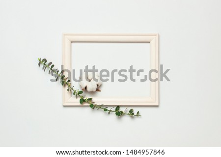 White wooden photo frame and spring green twigs of plants on gray background. Flat lay top view copy space. Stylish minimal composition, artwork mockup, picture frame, home decoration