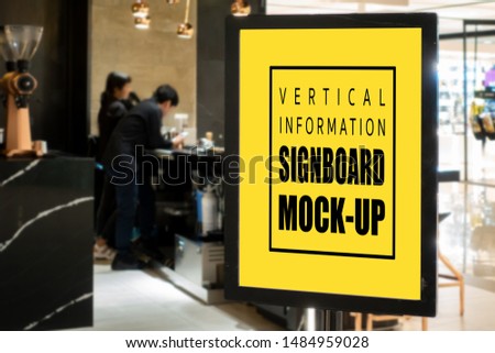 Mock up vertical blank signboard with clipping path in black frame at the cafe entrance, blurred people standing at counter, empty space for information and advertising