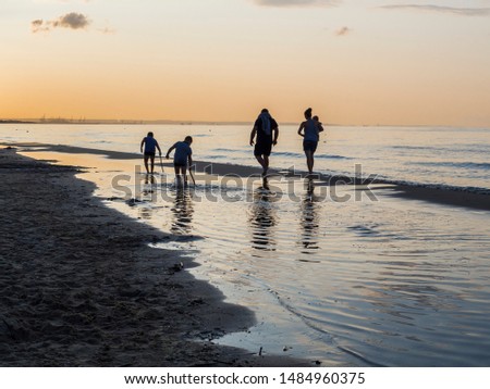Friendly family walks along the picturesque beach during sunset. Silhouette of a group of people on a background of sunset at sea. Beautiful summer sunset on the Polish coast of the Baltic Sea
