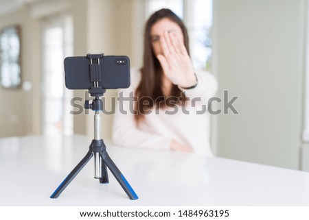 Beautiful young woman recording selfie video with smartphone webcam with open hand doing stop sign with serious and confident expression, defense gesture