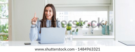 Wide angle picture of beautiful young woman working or studying using laptop surprised with an idea or question pointing finger with happy face, number one