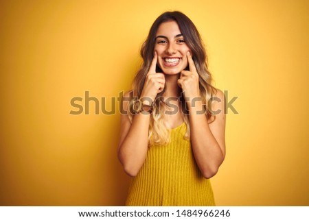 Young beautiful woman wearing t-shirt over yellow isolated background Smiling with open mouth, fingers pointing and forcing cheerful smile Royalty-Free Stock Photo #1484966246