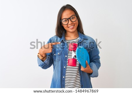 Young chinese student woman wearing glasses holding skate over isolated white background very happy pointing with hand and finger