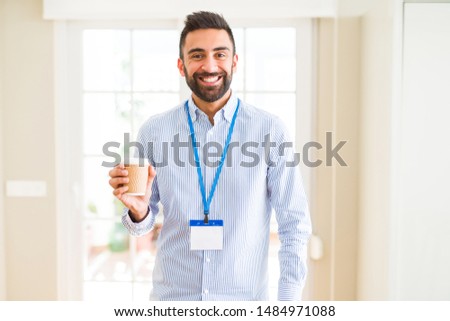 Handsome hispanic man wearing id card and drinking a cup of coffee with a happy face standing and smiling with a confident smile showing teeth