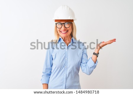 Middle age architect woman wearing glasses and helmet over isolated white background smiling cheerful presenting and pointing with palm of hand looking at the camera.