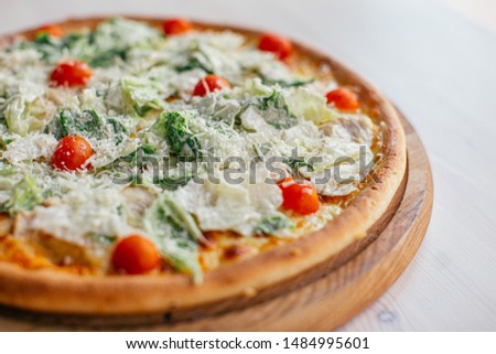 Fresh delicious Pizza with letucce and cherry tomatoes with white souse on wooden plate on white wooden table, side view