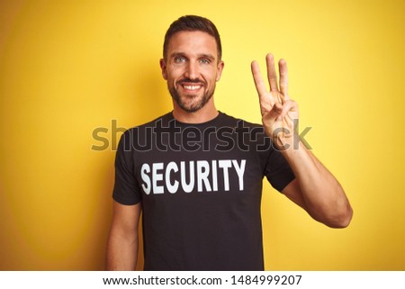Young safeguard man wearing security uniform over yellow isolated background showing and pointing up with fingers number three while smiling confident and happy.