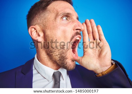 Close up picture of young handsome business man over blue isolated background shouting and screaming loud to side with hand on mouth. Communication concept.
