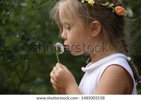 Little girl with flower wreath blowing on a dandelion