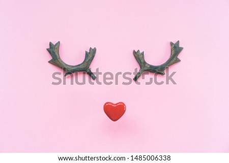 Funny muzzle made of ceramic red heart and wooden reindeer horns on a pink pastel background. Minimalism holiday concept. Flat lay top view composition