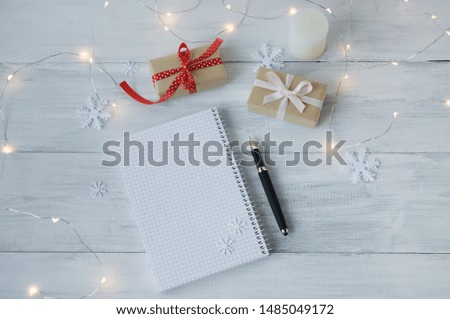 Two gift boxes, pen, notebook on white wood background. Presents in craft paper decorated with red and pink ribbon bows. Christmas and other holidays concept, top view, preparation for the holiday.