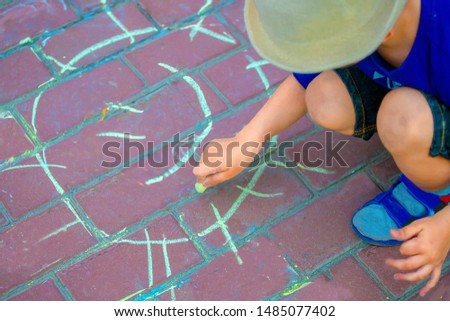 Little boy in a white hat draws a yellow chalk sun on a stone pavement
