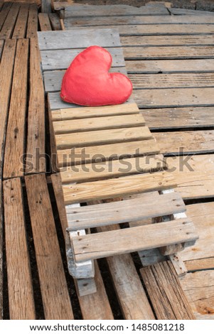 View of a wooden bench with a red heart pillow on a wood floor. Wood Patterns. Wooden slats.