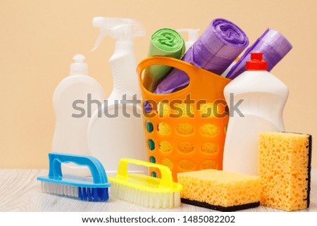 Plastic bottles of glass and tile cleaner, orange basket with garbage bags, sponges, brushes on beige background. Washing and cleaning set.