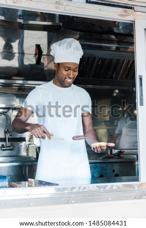 cheerful afrian american man holding spatula while preparing burger 