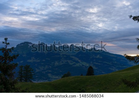 A mountain range and a green hill with some trees under a dramatic sky - colorful nature