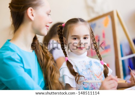 Little girl painting with teacher at kindergarten