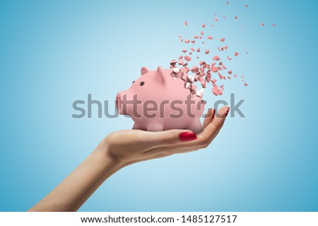 Close-up of woman's hand facing up and holding cute pink piggy bank that has started to disintegrate into pieces on light-blue background. Money worries. Financial difficulties. Profit loss. Royalty-Free Stock Photo #1485127517