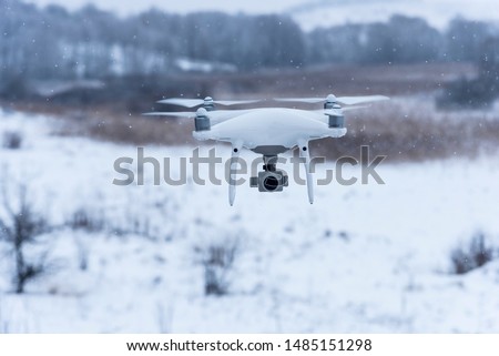 Hovering drone taking pictures of wild nature. Cold winter weather. Cloudy day with falling snow.