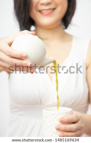 Asian woman are pouring hot green tea from the teapot into a white tea cup. Focus on the hand. Culture showing hospitality, picture show on the restaurant menu, drinking tea for health concept. Smile
