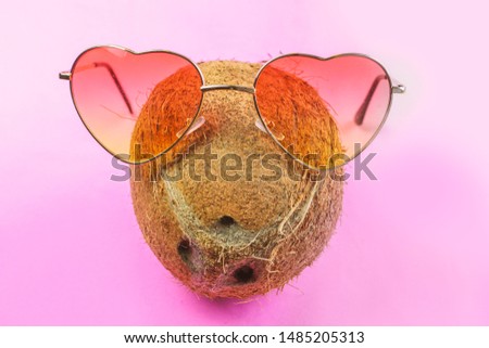 Coconut with black straw on neon bright pink background in vaporwave webpunk style, with heart-shaped glasses on it. Summer concept tropical flat lay. Fashion minimalism surrealism in fruits  