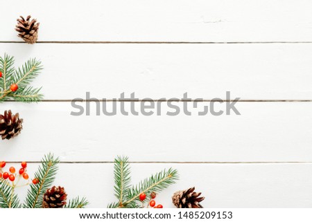 Christmas frame made of fir tree branches, red berries, pine cones on rustic wooden white desk. Christmas, New Year, winter holidays concept. Flat lay, top view, copy space