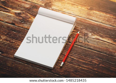 Notebook with a red pencil on a brown background with warm sunlight, for writing. Free empty space for writing on a blank sheet of a notebook.