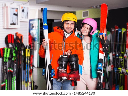 Cheerful young pair in skiing outfit satisfied with choice in modern shop of sports equipment