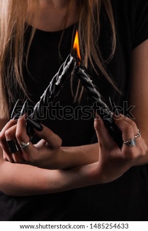 Female hands with long nails hold burning candles on a black isolated background. concept of witchcraft witchcraft on halloween. silver rings on the fingers.