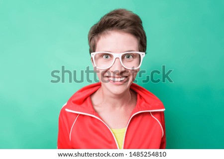 Close-up portrait of a funny young attractive woman in red tracksuit and white glasses isolated on green background. Cute toothy smile.