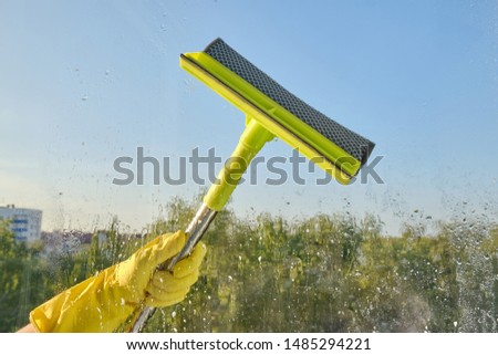 Female hand in yellow gloves washes a window with a window scraper