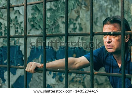 A depressed man in handcuffs behind bars. A depressed arrested male offender is jailed. Shouts, breaks, cries.