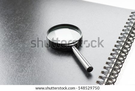 Black magnifying glass on black notebook, angle view, office background