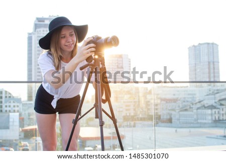 young girl photographer with a camera and a tripod on a background of the city, she photographs at sunset, a woman shoots a video