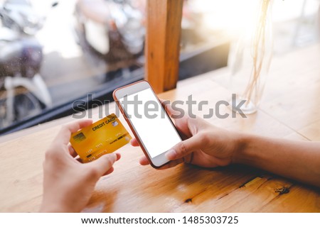 Close up of man using blank cell phone and credit card sending massages shopping online or reporting lost card, fraudulent transaction in the coffee shop.