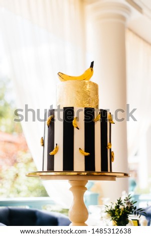 Big stripped round cake decorated with gold and bananas on it. Outdoor composition.  
