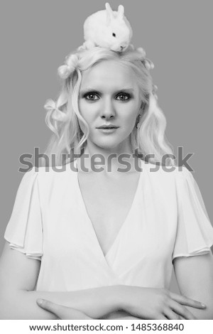 Fashion portrait of albino blond girl with white skin and blue eyes in elegant dress posing with cute little rabbit on gray background in studio