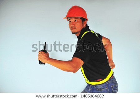 Worker holding a walkie talkie and wearing safety vest run over on soft blue background.