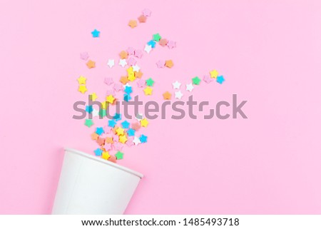 Drinking paper cup with multi-colored confetti scattered on a pink background. Flat composition Birthday celebration, Merry Atmosphere. Greeting card poster template. Copy space