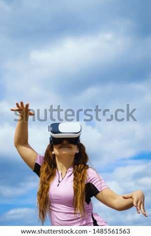 Young woman testing VR glasses outside. Female wearing virtual reality headset during summer weather