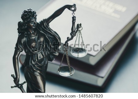 Statue of the figure of Justice holding scales and a sword high angle against law books in court symbolic of the law