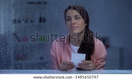 Sad woman with photo feeling sad behind rainy window, remembering first love