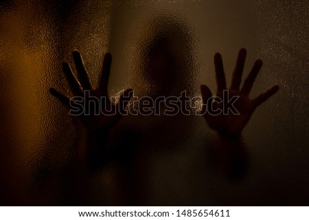 Silhouette scared woman hands behind glass window. Concept horror background.